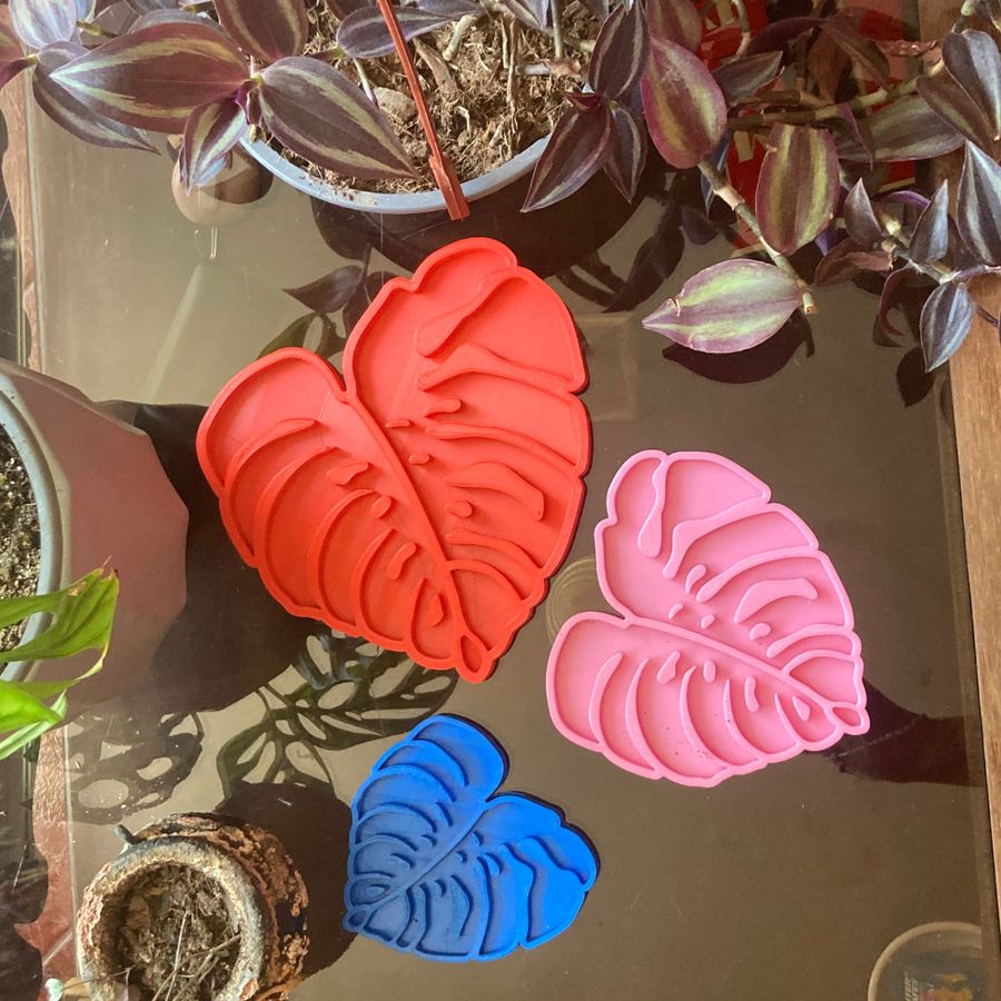 Tres hojas de monstera impresas en 3D en rojo, rosado y azul